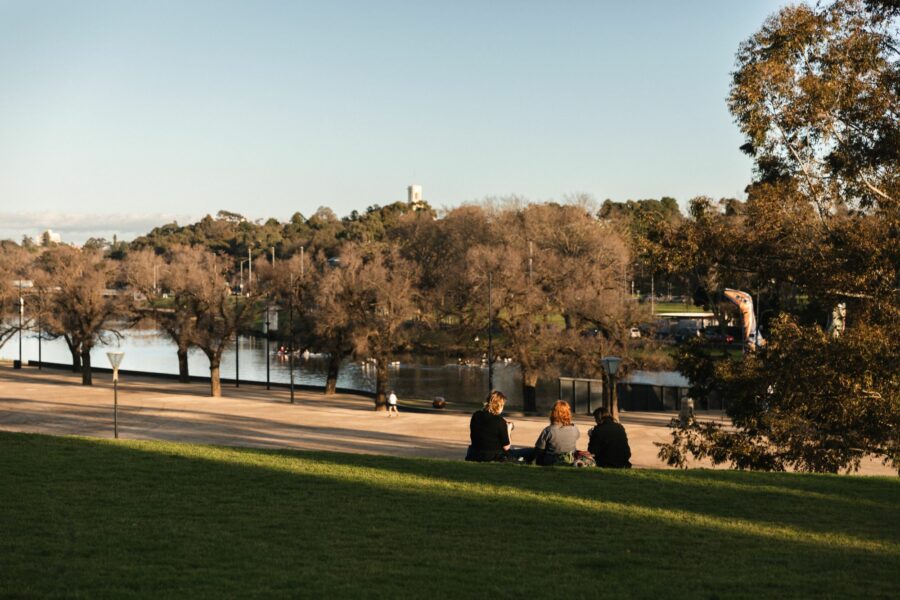 Three people sitting on the banks of the Yarra River, Birrarung