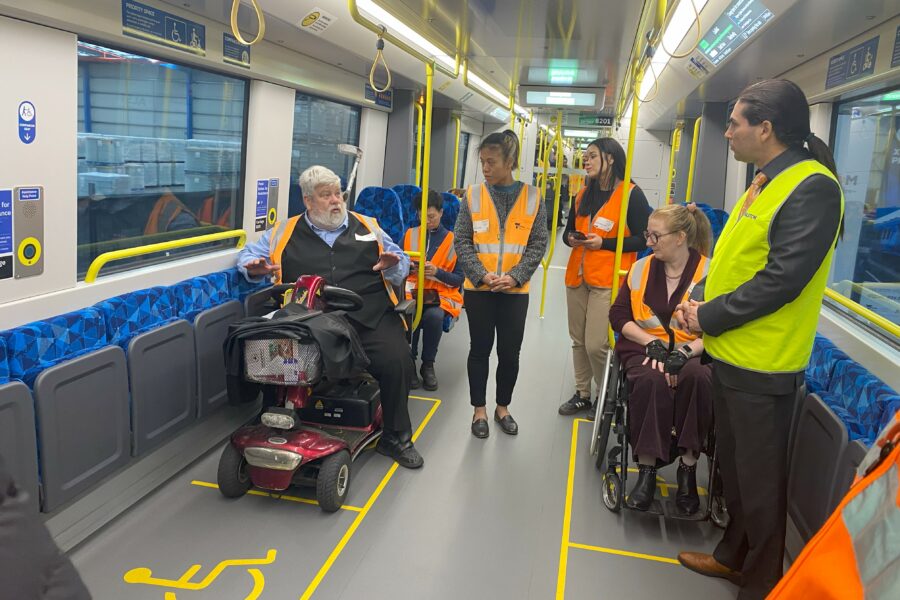 A community engagement session on the mock-up X’Trapolis 2.0 train. Wheelchair users test the new train; facilitators stand in the aisle