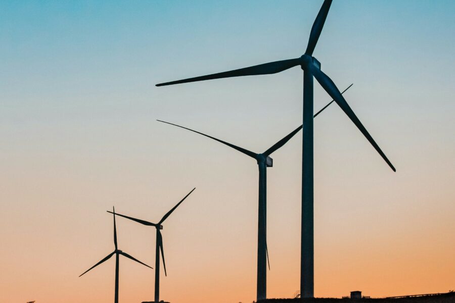 A group of wind turbines, silhouetted against a setting sun. The sky is blue and orange.