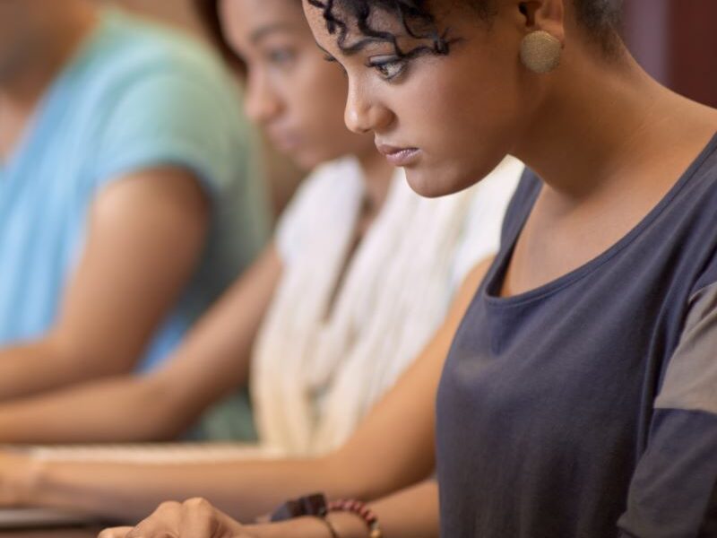 A group of students seated at a table, working on laptops.
