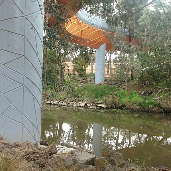 Pedestrian bridge winding across Werribee River to Wyndham Park, surrounded by trees