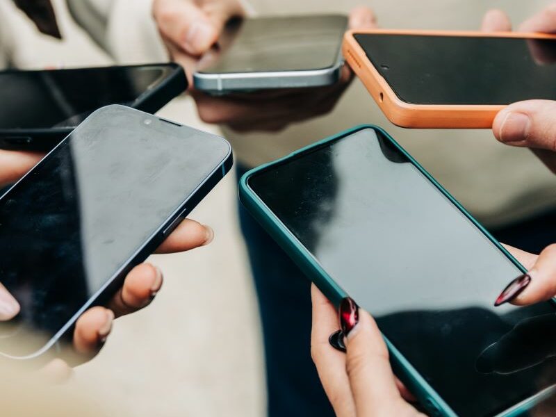 Close view of young people's hands holding mobile phones in a circle, browsing together.
