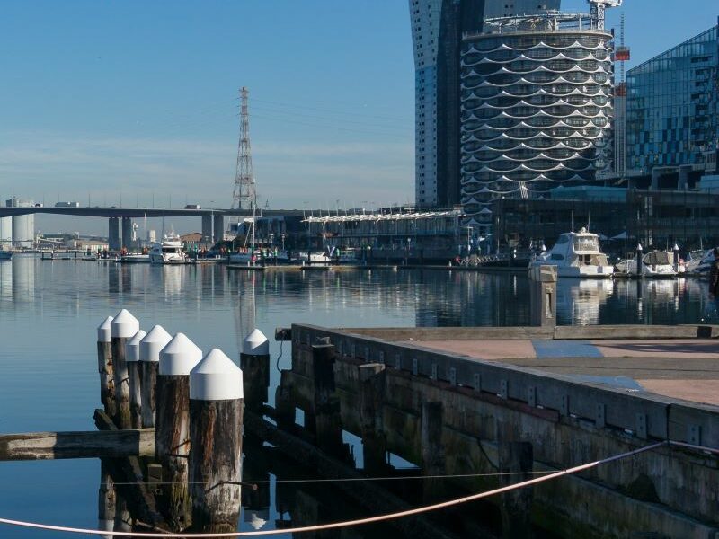 The Docklands waterfront. Central Pier and a yacht in the water; a bridge and buildings set against a clear blue sky in background