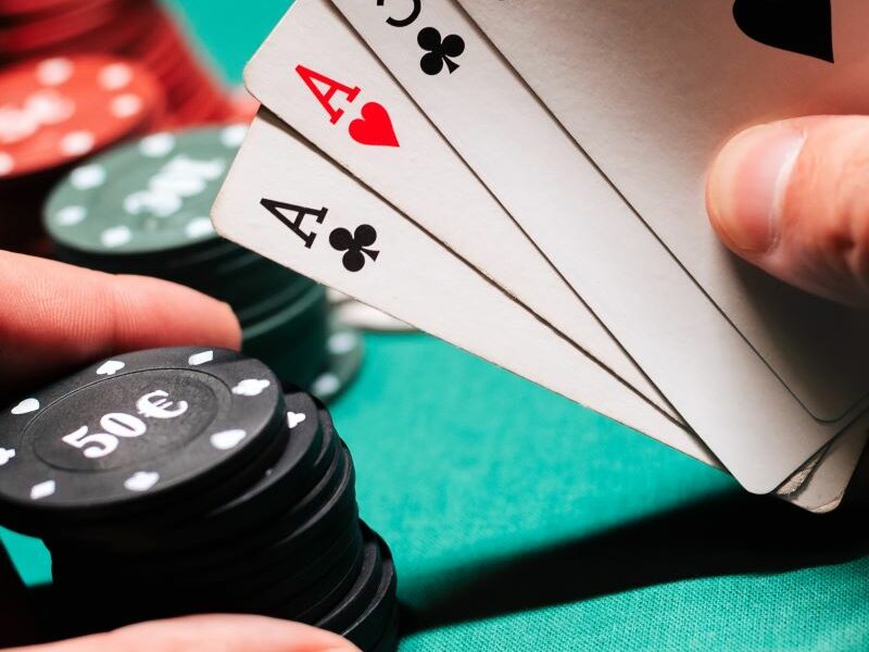 Two hands holding playing cards on right and poker chips on left.