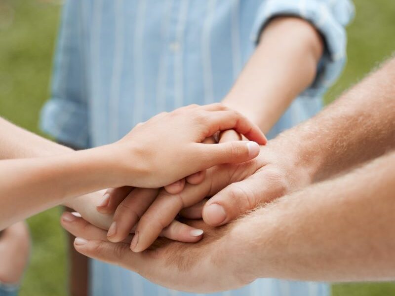 A hand stack. A group of three people stand in a circle (faces not visible); their hands are stacked in the centre
