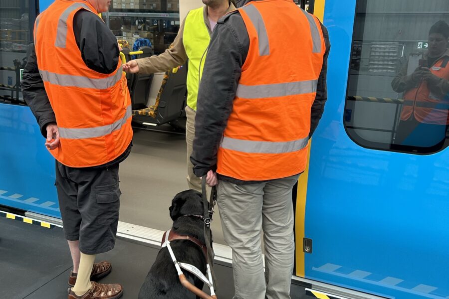 Two men, one with a guide dog, waiting to board the train