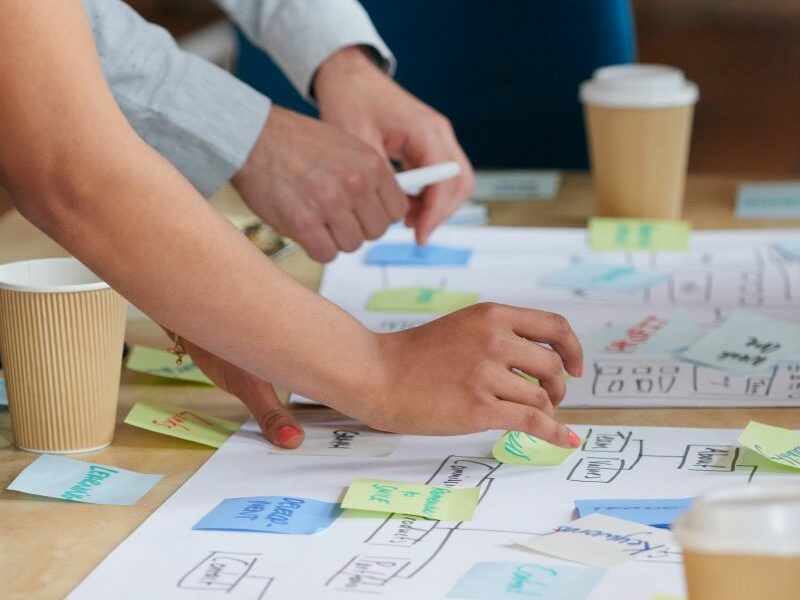 A community focus group. Worksheets covered in Post-it notes and take-away coffee cups on table; people, only partially visible, gathered around
