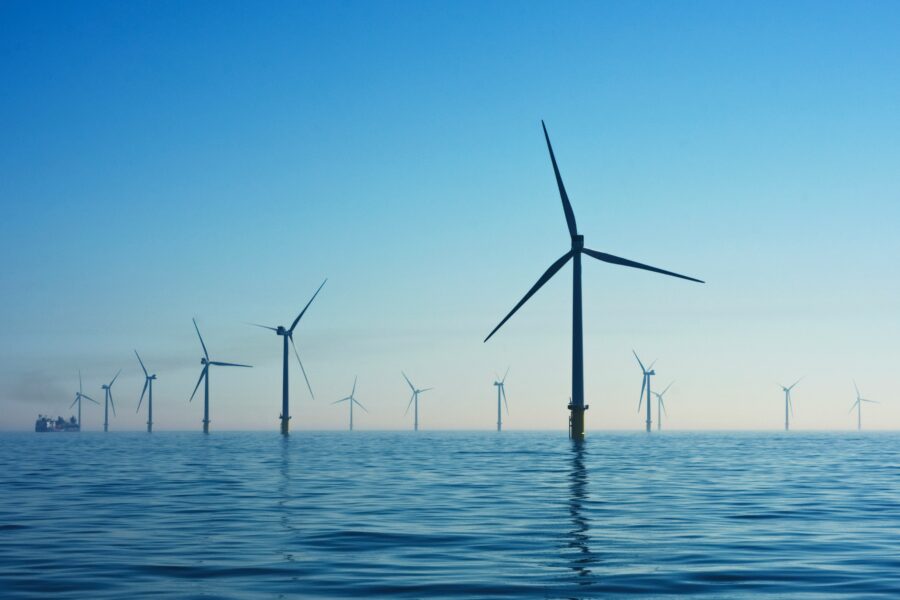 An offshore wind farm; wind turbines appear against a blue sky and deeper blue ocean