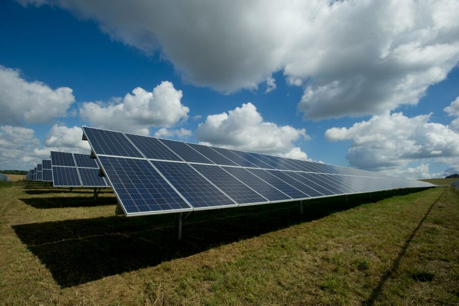 A field of solar panels. Green grass below; blue sky with large cartoonish clouds above