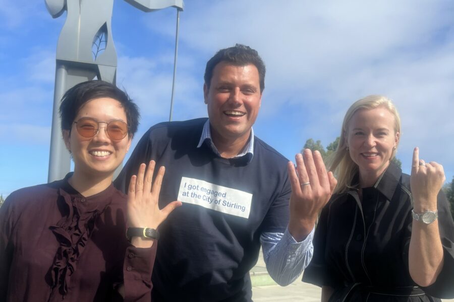 Two Capire Associates standing either side of a City of Stirling representative. They are wearing 'engagement' rings and standing outside, in front of a statue