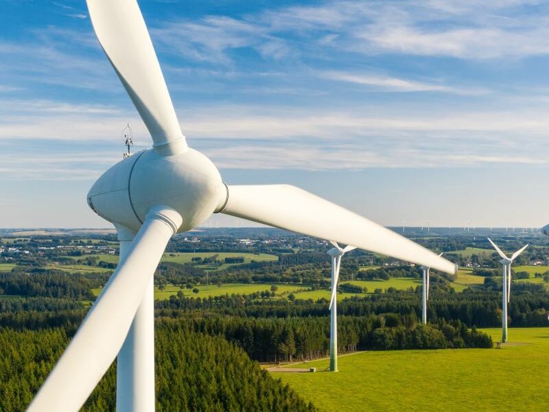 Wind turbines in a rural area. Green grass and trees below, cloudy blue sky above