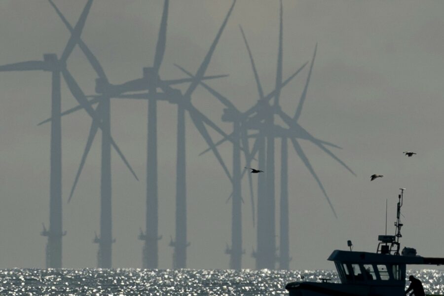 Silhouette of a boat on the water, wind turbines in background, birds flying overhead
