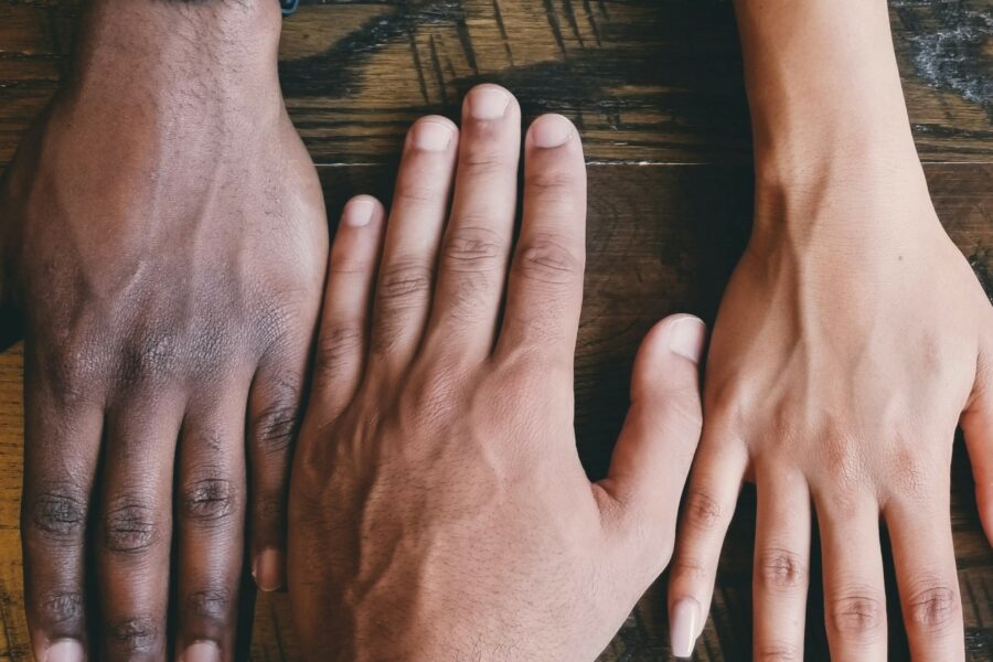 Three hands with different skin tones laid together on a wooden table