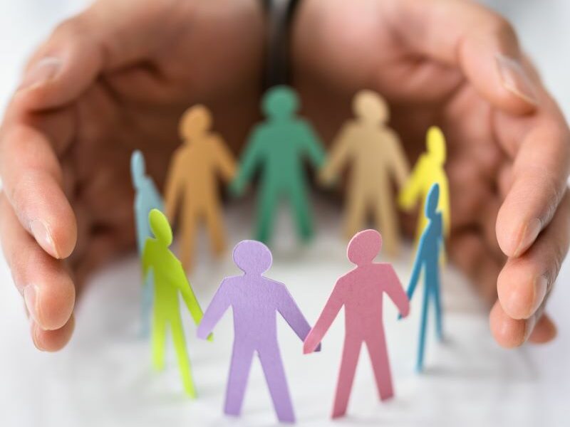 Colourful paper dolls standing in a circle. In the background, a person's hands are cupped around the paper people