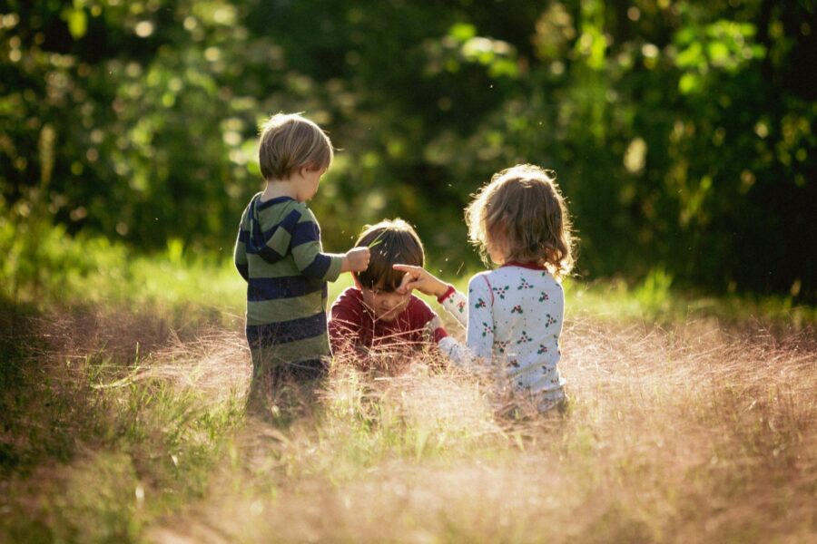 Three children playing in a field; trees in background